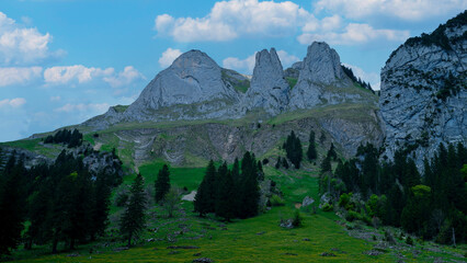 Scenic mountain landscape with towering peaks and lush greenery under a blue sky filled with fluffy clouds