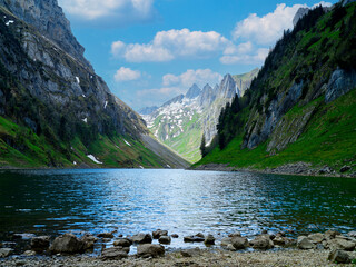 Scenic mountain lake surrounded by green hills and rocky cliffs under a blue sky with clouds