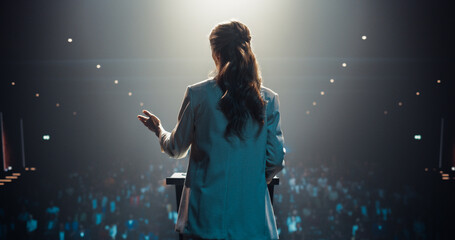 Businesswoman Walking Out on Stage to Give a Talk at a Global Finance Summit. Audience Listening to Her Insightful Talk. Speaker Standing with Her Back to Camera While Making a Motivational Speech