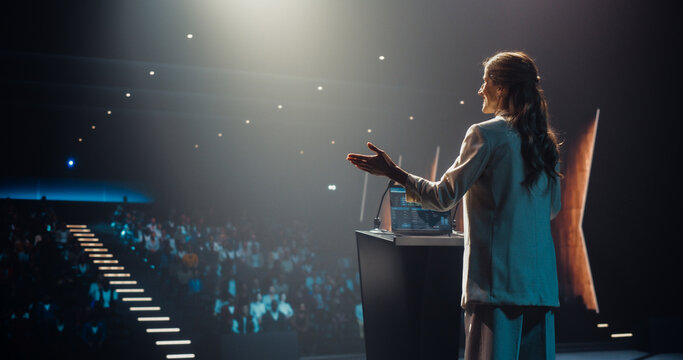 Excited Female Entrepreneur Shares an Insightful Talk on Technology and Leadership at a Professional Business Conference. Diverse Multiethnic Guests Sitting in a Dark Auditorium