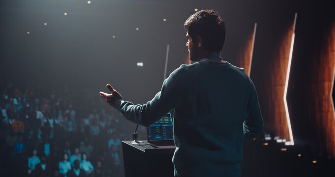 Indian Business Leader Giving a Talk on Stage at a Global Finance Summit. Audience Listening to an Insightful Talk. Speaker Standing with His Back to Camera While Making a Motivational Speech