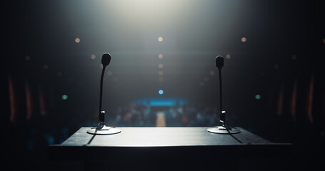 Two Microphones on a Podium Stand. Establishing Shot Before a Keynote Speech on a Dark Stage, Set Against a Backdrop of a Blurred Diverse Audience. Significant Event at a Public Speaking Venue