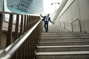 Happy mature business man dancing walking on stairs in front of office building outdoors