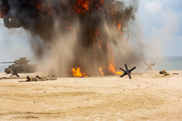 World War II historical reconstruction. Battlefield. Explosions, a tank, and American soldiers on the beach. Smok and dust.