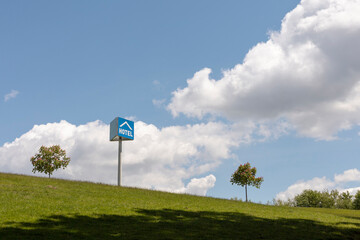 A bright blue hotel sign is positioned on a grassy slope, surrounded by small trees, beneath a...