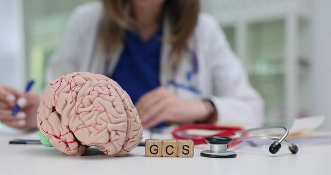 Abbreviation GCS of wooden cubes near brain model and stethoscope against doctor. Woman therapist suggests disorder treatment of neurological function