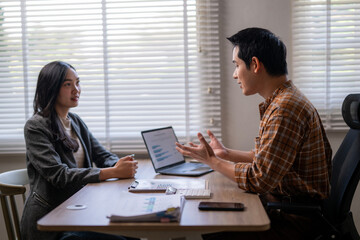 A man and a woman are sitting at a table with a laptop and a cell phone