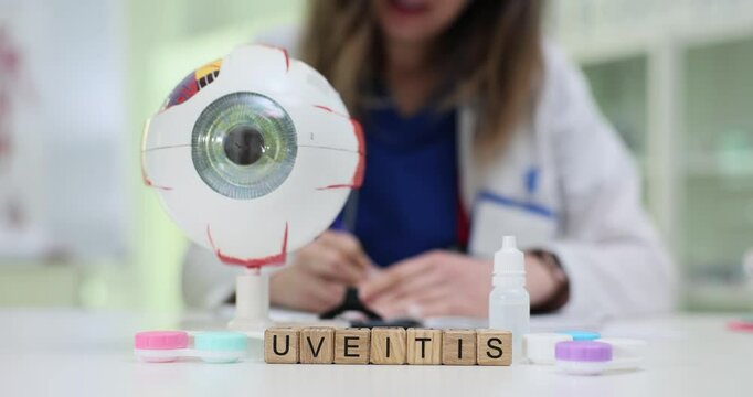 Woman analyzes eye anatomical model discussing Uveitis treatment near wooden cubes. Professional works in ophthalmology examination room slow motion