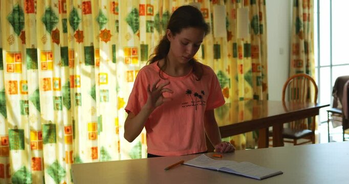 Motivated brunette reviews jottings practicing finger language movements. Long-haired lady stands at table attentively looking at notepad learning to be interpreter