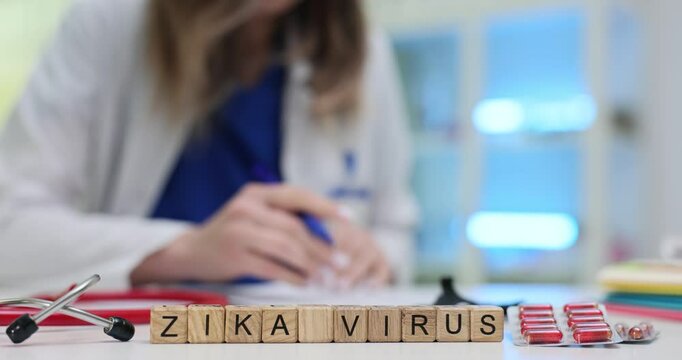 Female professional writes prescription near wooden cubes with Zika Virus surrounded by red capsules. Urgent medical intervention for viral infection