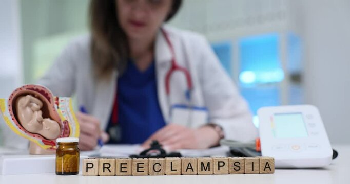 Medical professional documents patient information against cubes with Preeclampsia and tonometer. Anatomical pregnant uterus model near medication