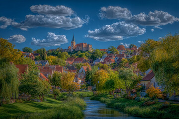 an old town in high contrast, a horizontal angle shot of a castle and buildings. The walls are a golden yellow with red roofs, set against a beautiful blue sky with white clouds
