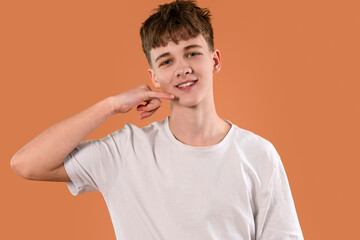 Teen boy smiling while gesturing call me with hand on an orange background during a casual indoor...