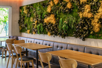 Cozy cafe features a stylish interior with wooden tables and chairs, complemented by a vibrant green wall adorned with various plants, creating an inviting atmosphere for guests