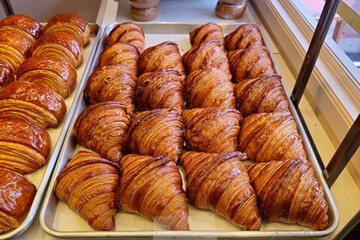 Freshly baked golden brown croissants arranged neatly on metal trays inside a bakery display