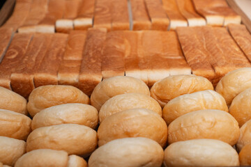Rows of fresh plain buns and sliced bread arranged neatly in a wooden tray. Soft texture and...