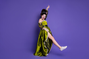 Young woman dressed in vintage-style green gown with white sneakers against a vibrant purple...