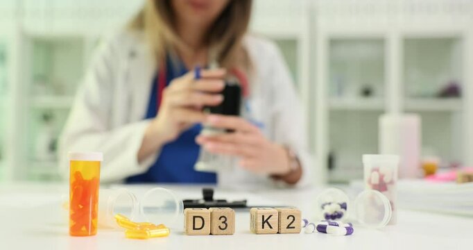 Inscription vitamins D3 and K2 on wooden blocks near capsules against working doctor. Woman doctor promotes patient health and wellbeing in clinic