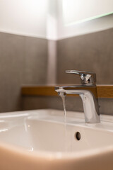 Fototapeta premium A sleek faucet pours water into a pristine sink, showcasing modern bathroom design. The setting is bright and minimalist, highlighting the simplicity and elegance of the space