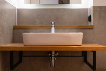 A stylish bathroom features a white rectangular sink perched on a warm wooden countertop. Clean lines and minimal decor highlight a contemporary aesthetic. Soft lighting enhances the ambiance