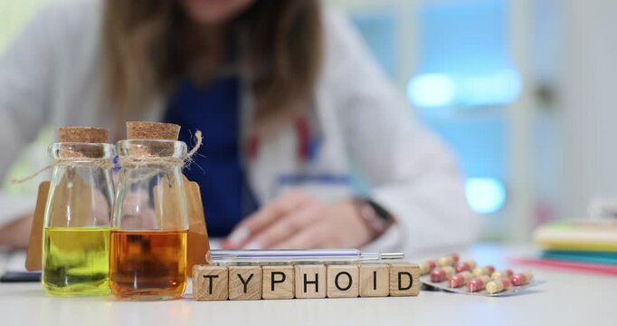 Female doctor writes prescriptions at table with inscription Typhoid and yellow and orange liquid. Focus on infectious disease treatment in clinic
