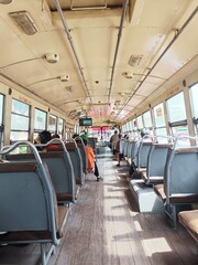 interior of a bus. Thai buses in Bangkok are non-air-conditioned buses with windows open on all sides and passengers sitting in empty seats.