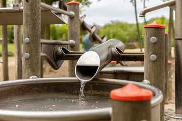 Children's playground features a water chute with flowing water, surrounded by wooden structures....