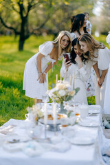 A group of women dressed in elegant white dresses are gathered around a table