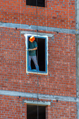 A man plasters a window opening in a building under construction on a spring day