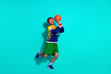 Dynamic young athlete in colorful retro sportswear posing actively with a basketball against a vibrant turquoise background