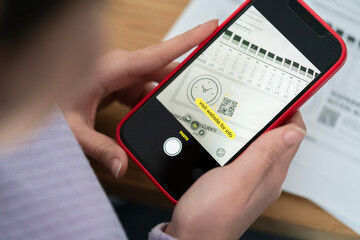 Person holds smartphone scanning a QR code on a document displaying business data. The phone screen shows a prompt to visit a website for information.