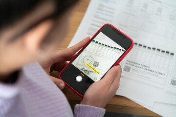 Close-up of a person holding a smartphone, scanning a QR code on a paper document. This illustrates modern digital methods for accessing information or making payments.