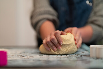Person kneading dough on a floured surface. Hands covered in flour work the dough. Preparing for baking or cooking. Close up view of the process.
