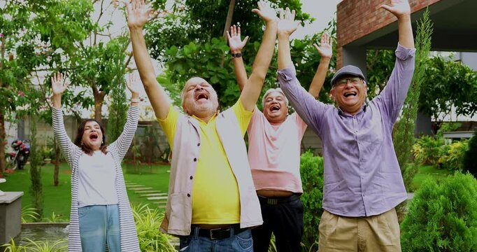 Seniors enjoying in laughter club outdoors, Indian Asian old age friends standing in lush green garden bursting in laughter with positive expressions in morning healthy activity