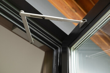 Close-up of a modern door closer mechanism in an open aluminum-framed window, showing construction detail and engineering design.