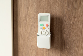 White remote control in a wall holder mounted on a wooden surface, used for air conditioning or home devices.