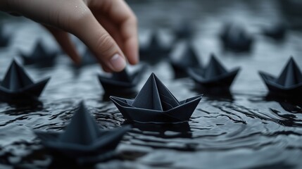 Hand placing black origami paper boats on rippling water surface creating a somber and reflective scene