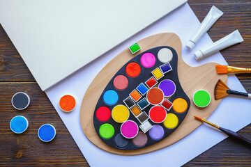 Palette, paper for watercolor painting, colorful watercolor paints and paintbrushes. Copy space