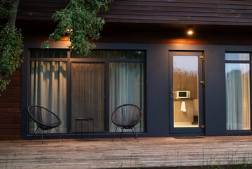 Modern wooden house exterior with two chairs and warm evening lights on the terrace.