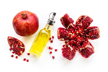 Pomegranate seed oil in a glass bottle and fresh fruit on a table, top view