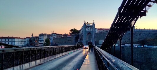 Fototapeta premium A twilight view of the iconic Sidi M’Cid Bridge in Constantine, Algeria, captured during the golden hour. The suspension bridge, illuminated by the fading sunlight and the soft glow of car headlights