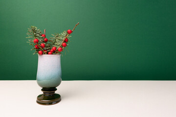 Nobilis fir and winterberry branches in a vintage vase in front of green background.