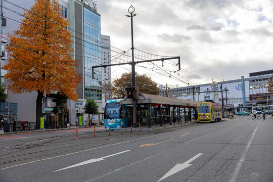 Okayama City, Japan - December 2024: Wide view of the urban area in front of Okayama Station, the central transportation hub of. The scene includes city buildings, local buses, trams, and pedestrians 