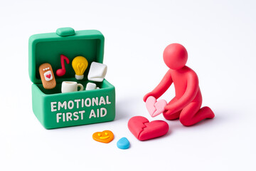 Small figurine kneels ground holding heart shaped object with box labeled emotional first aid nearby, symbolizing mental health support