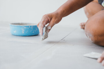 Hand gripping a rubber float tool while pressing grout into the spaces between ceramic floor tiles. Close-up showing seamless tile work.