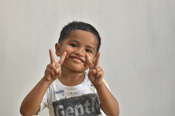close up of 3 year old boy raising two fingers while smiling, on white background