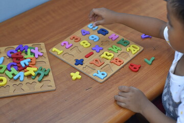 Close up of a 4 year old boy's hands playing an alphabet puzzle on a wooden table
