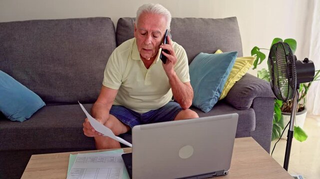 Video of Senior man managing domestic bills using laptop during hot weather while sitting on sofa
