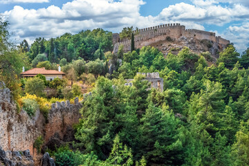 Fototapeta premium A picturesque view of Alanya Castle, surrounded by lush greenery and ancient stone walls under a partly cloudy sky, Turkey. The historic fortifications blend beautifully with the natural landscape
