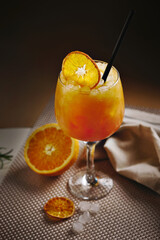 Close-up of vibrant orange cocktail served in a stemmed glass with crushed ice, dried orange slice, and straw